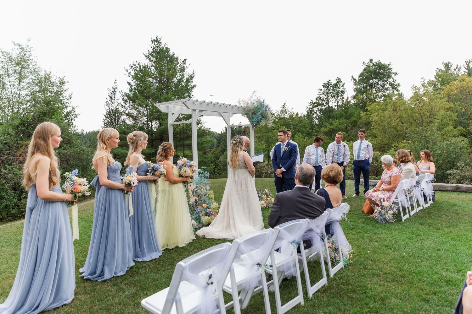 Outdoor wedding ceremony of bride and groom standing under an arch during their outdoor summer wedding near woodstock, ontario.