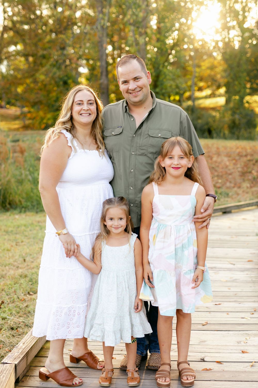 Happy family of four posing on a wooden bridge surrounded by autumn trees at golden hour.
