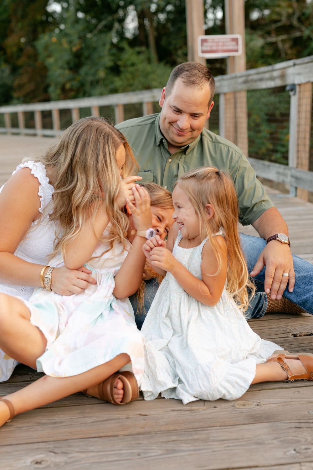 A happy family of four shares a playful moment sitting together on a sunny wooden boardwalk.