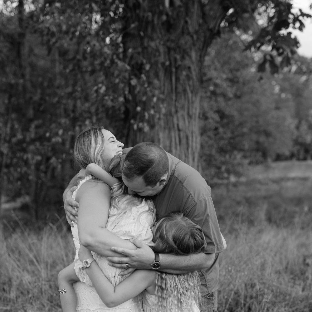 A family shares a tender group hug in a grassy field in this black and white portrait.