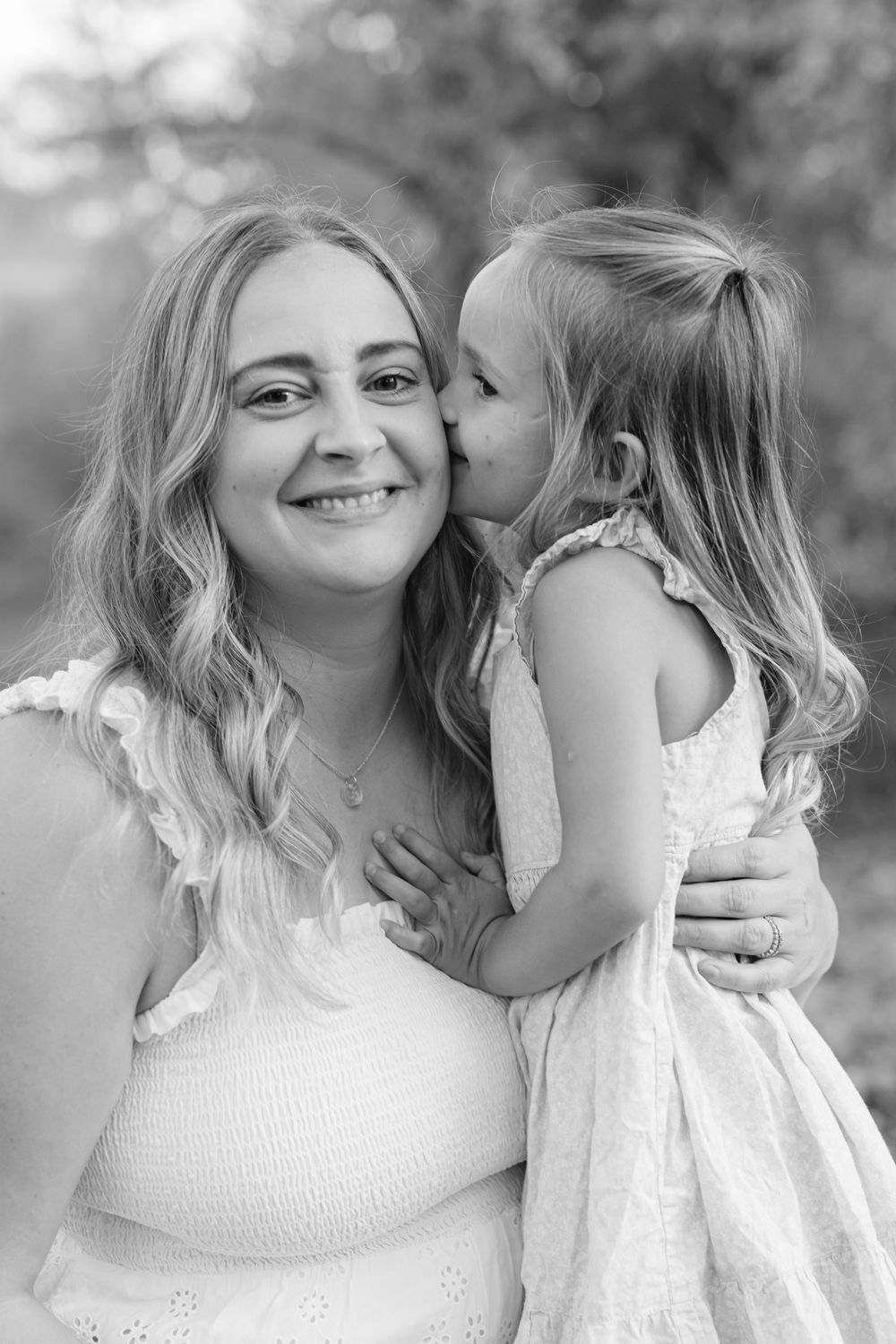 Black and white portrait of a young girl giving her smiling pregnant mother a sweet kiss on the cheek.