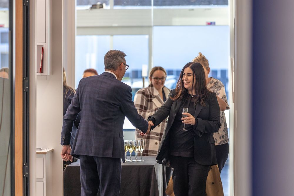 Professionals networking at a corporate event, shaking hands and holding wine glasses in a modern office space.