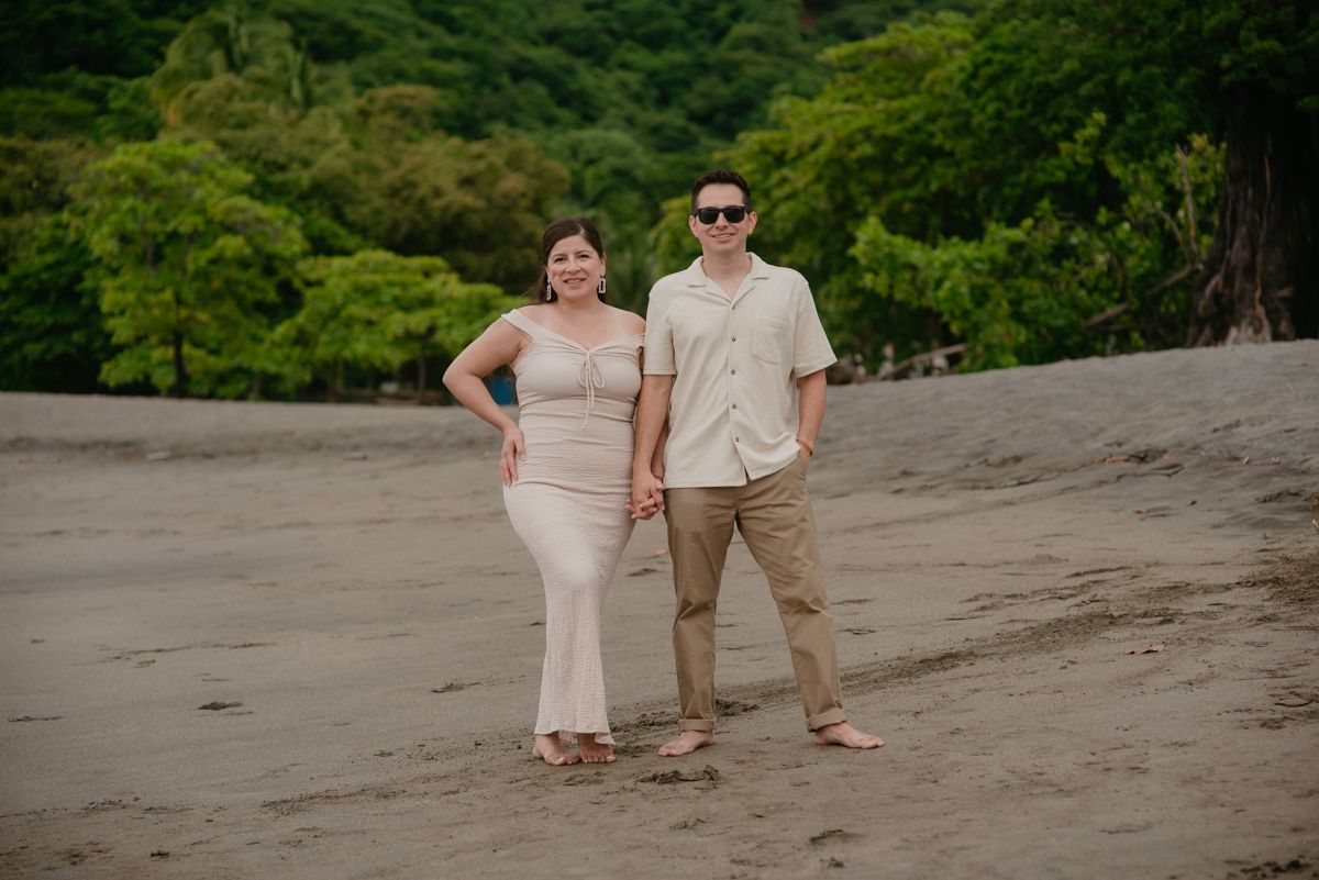 Two women in matching yellow dresses and sunglasses pose joyfully on a beach with ocean waves and blue sky.