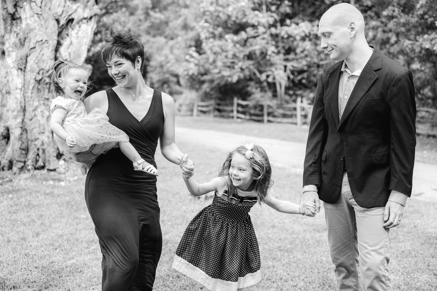 Multi-generational family walking together on a garden path, dressed in blue and white outfits, smiling outdoors.