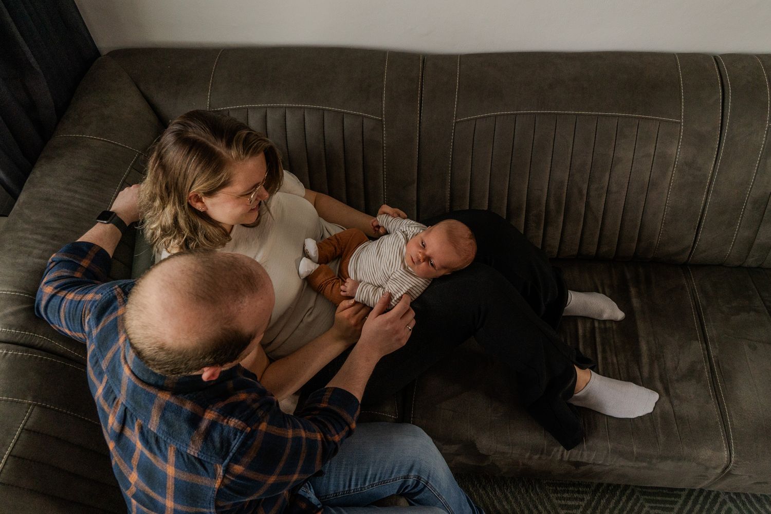Ouders die tijd doorbrengen met hun pasgeboren baby op een grijze bank, van bovenaf gezien, in een gezellig huis.