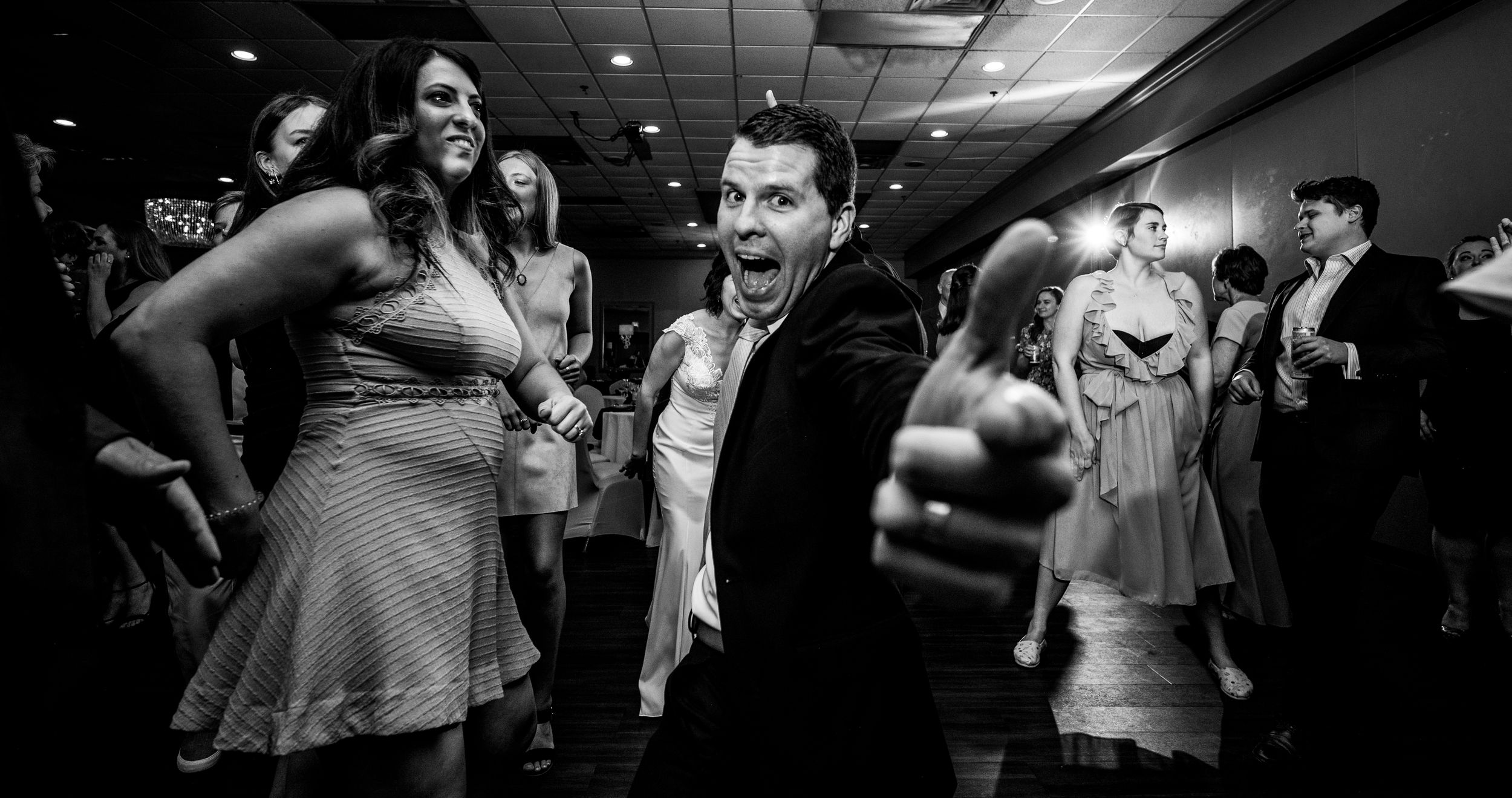 Black and white photo of guests dancing and celebrating joyfully at a wedding reception party.