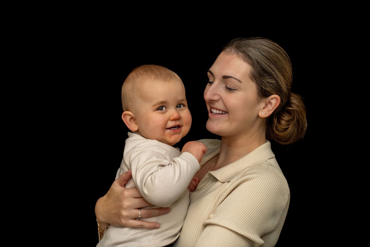 Een lachende moeder houdt haar blije baby vast tegen een zwarte achtergrond.