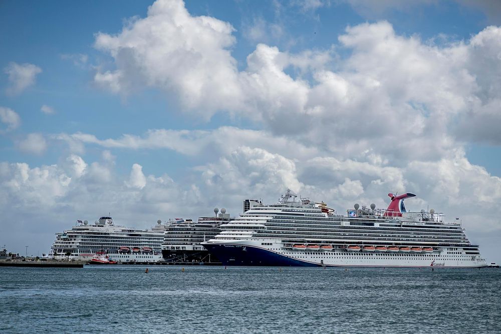 Two large cruise ships docked at port under a blue sky with fluffy white clouds.