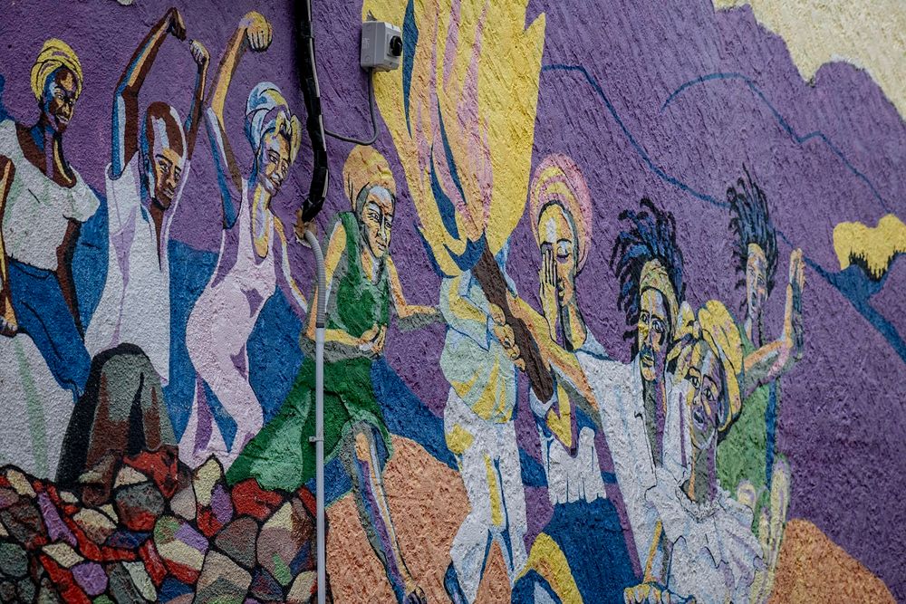 Vibrant mosaic mural depicting diverse figures dancing in colorful flowing garments on a textured wall.
