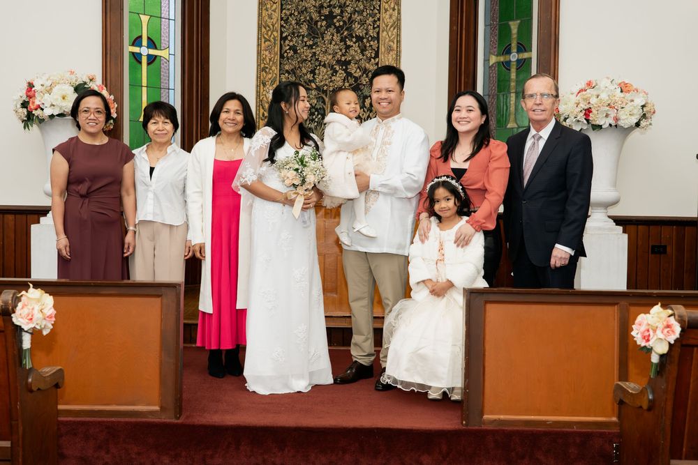 Wedding party poses together in church with floral arrangements, including children in white.