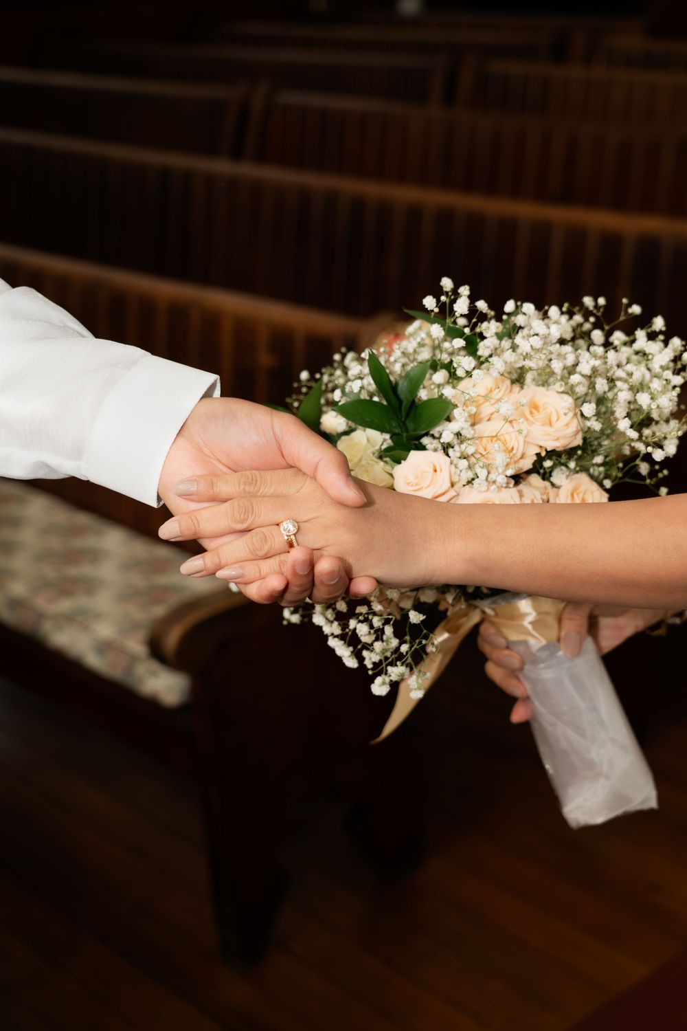 Bride and groom holding hands with a wedding bouquet of roses and baby's breath in a church.
