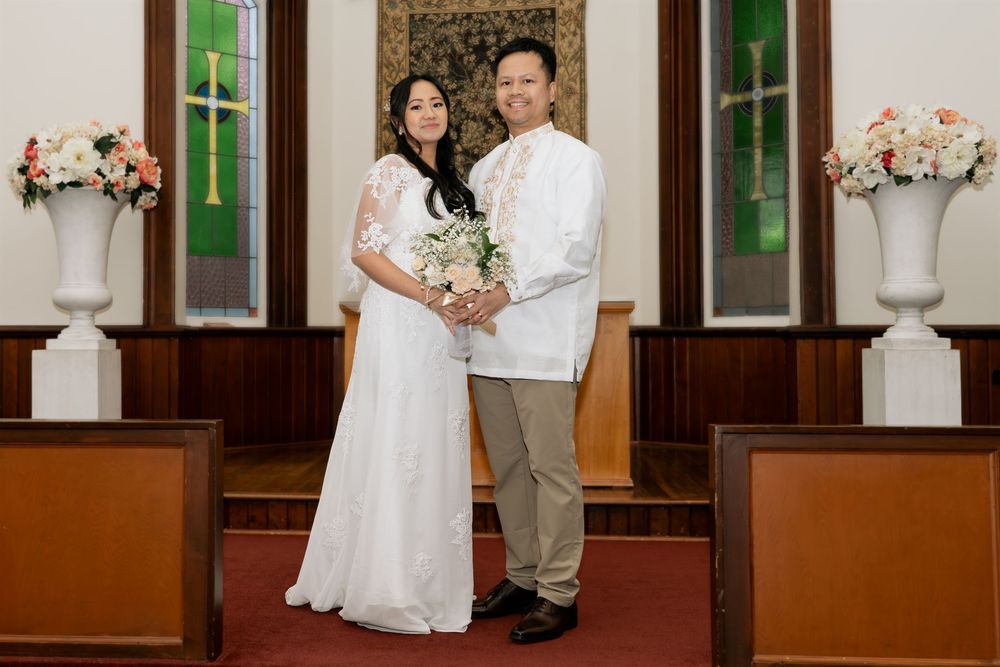 Newlywed couple posing together at the altar of a church decorated with pink floral arrangements.