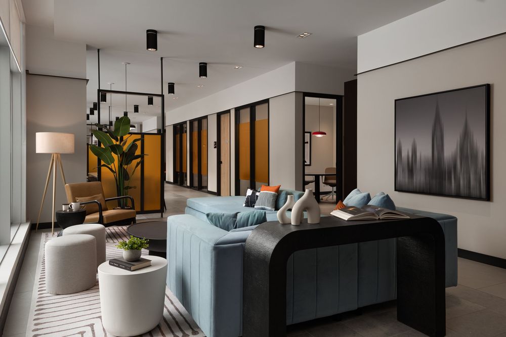 Modern hotel lobby with blue sofa, pendant lights, potted plant, and city skyline artwork in a sleek, contemporary design.