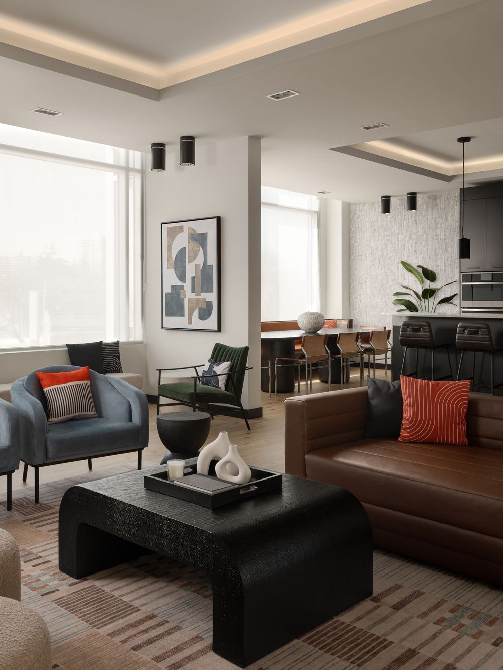 Modern open-plan living room with brown leather sofa, black coffee table, blue armchair, and dining area with pendant lights.