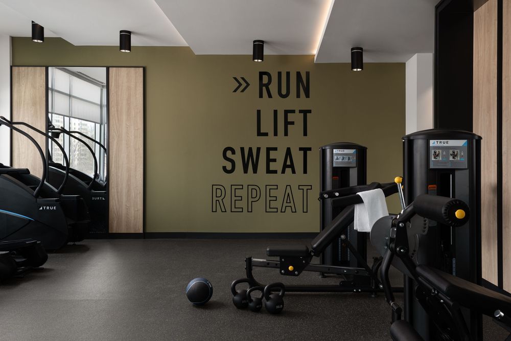 Modern hotel gym with motivational RUN LIFT SWEAT REPEAT wall art, featuring cardio machines and free weights.