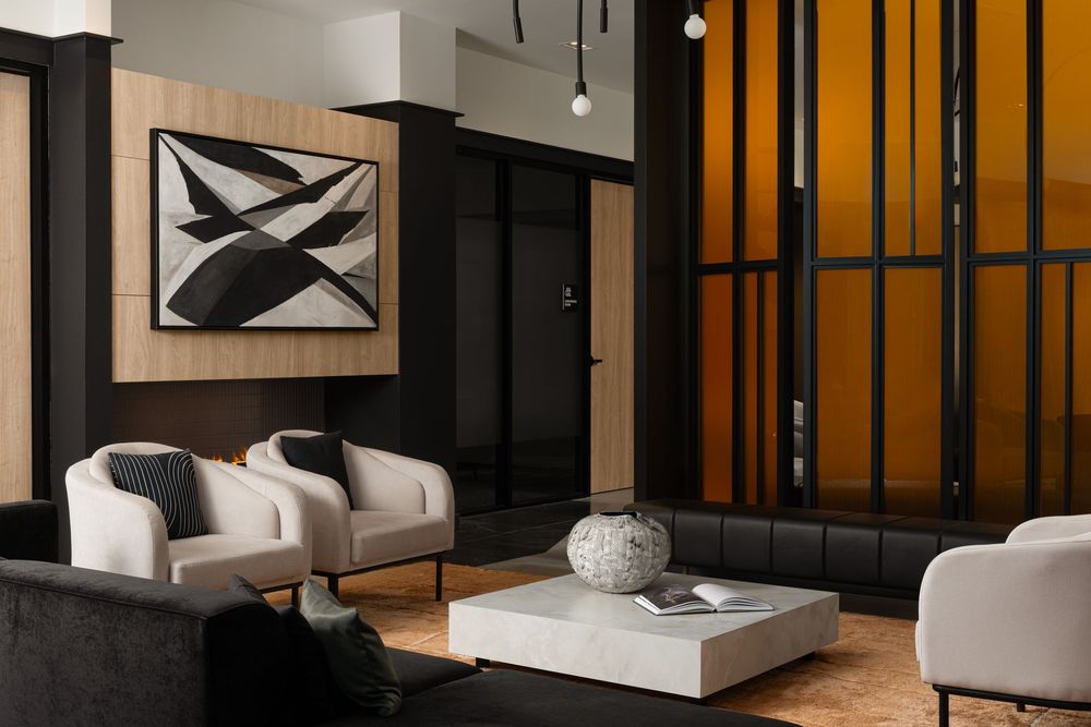 Modern lounge with white armchairs, abstract wall art, coffee table, and warm amber glass partition in elegant dark interior.