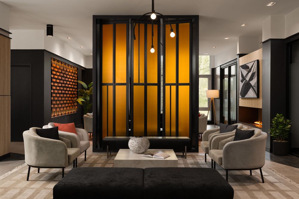 Modern hotel lobby with glowing amber partition, neutral armchairs, and contemporary artwork in a sophisticated dark interior.