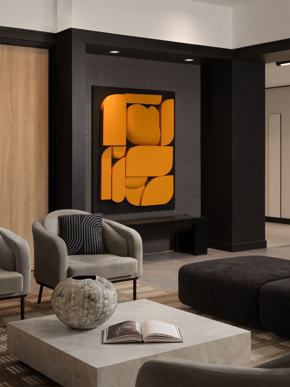 Modern lounge with gray armchairs, concrete coffee table, and bold orange abstract wall art in a dark interior.