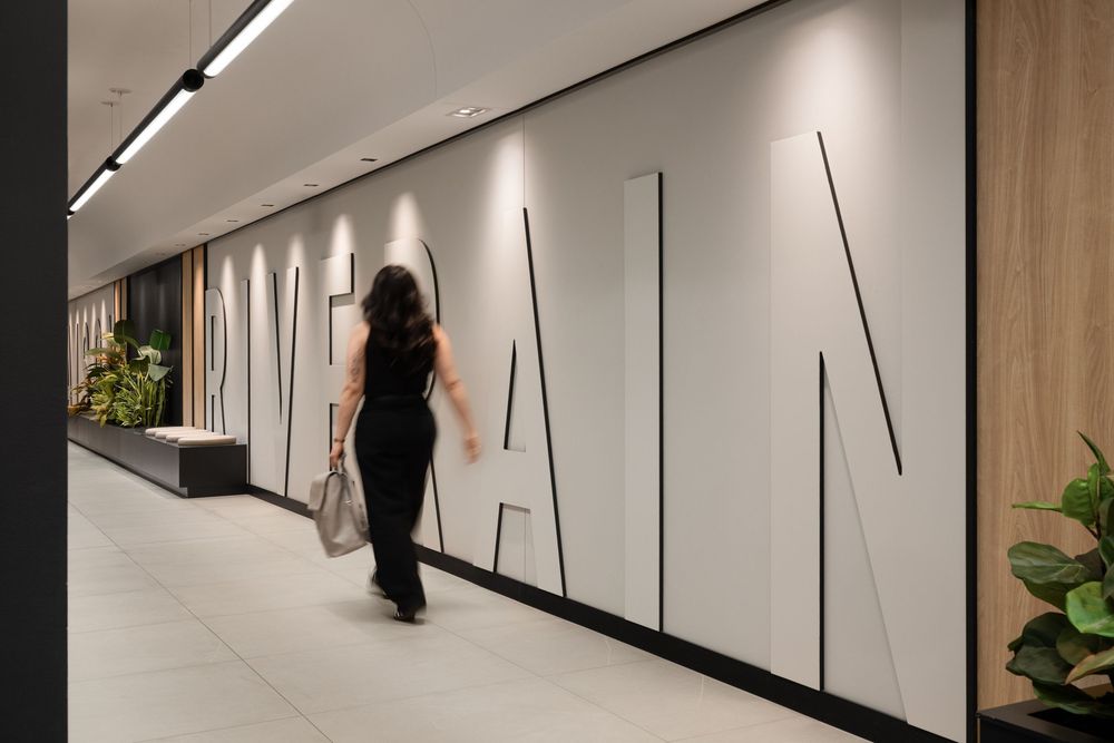 Woman walking through modern office corridor with large decorative lettering on white wall panels.