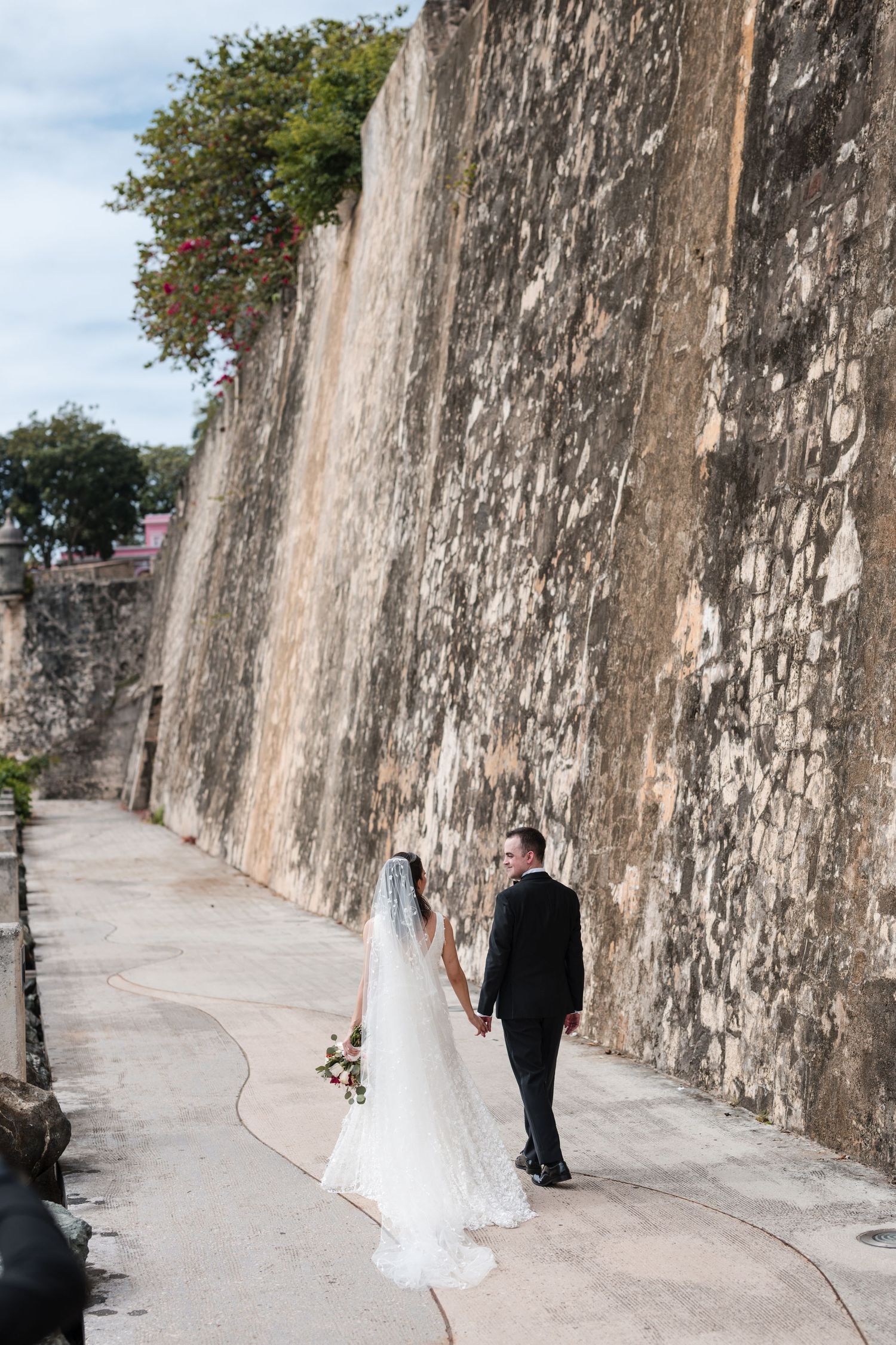 •	Couple walking along historic stone wall in Old San Juan