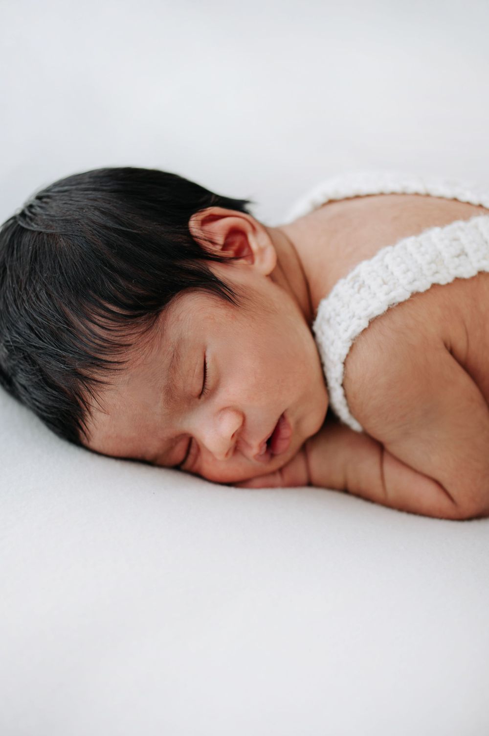Peaceful newborn baby sleeping on white background wearing white knit wrap.