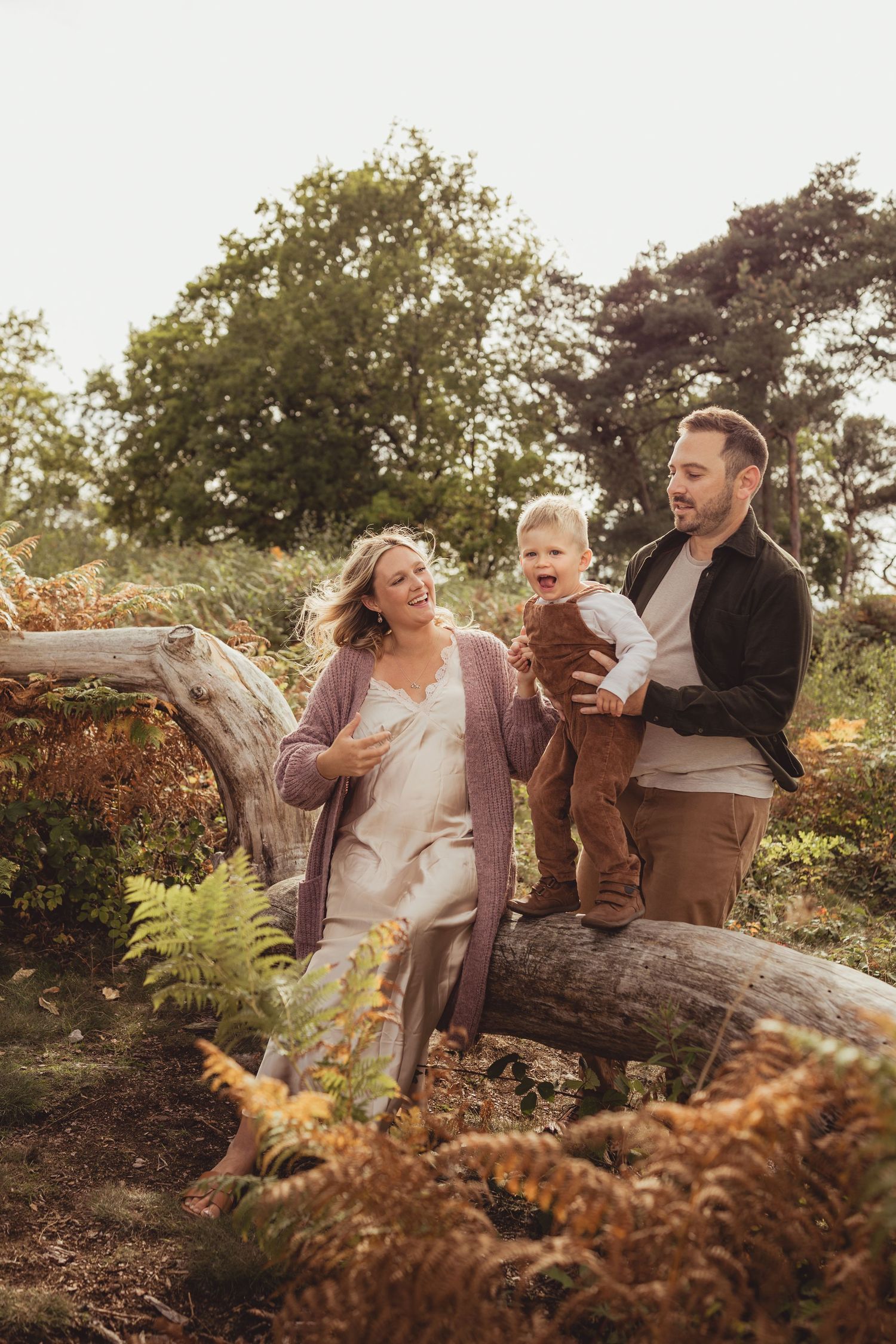 A happy family of three enjoys a sunny autumn day outdoors, with parents smiling at their toddler son.