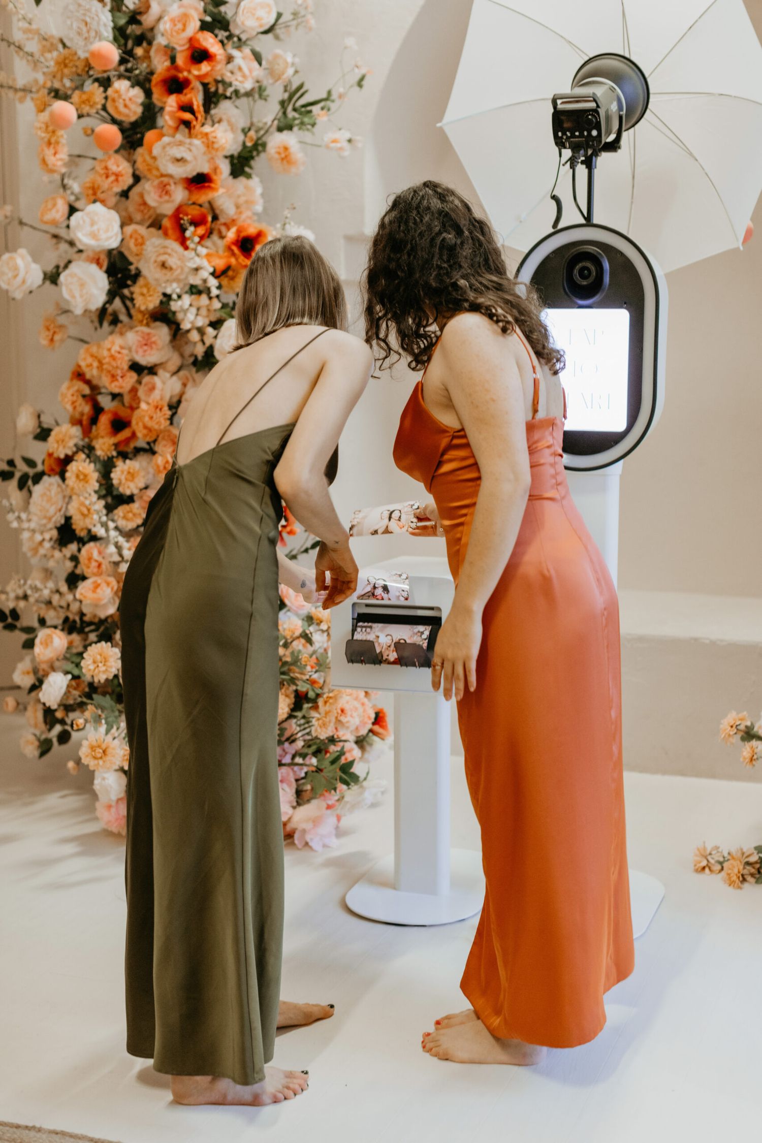 Elegant white photo booth setup with draped fabric backdrop, cocktail table, and professional lighting equipment.