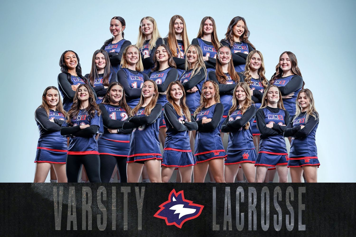 Varsity lacrosse team photo featuring young women in navy blue uniforms posing together for an official team portrait.