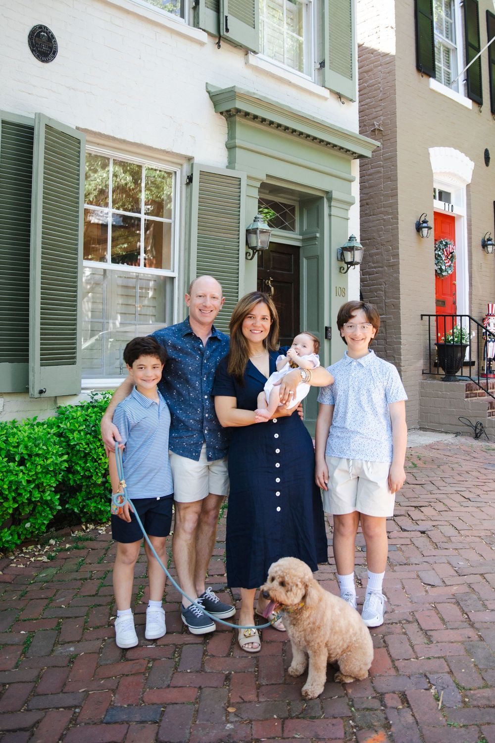 Happy family of five with a golden doodle dog posing in front of a charming townhouse.