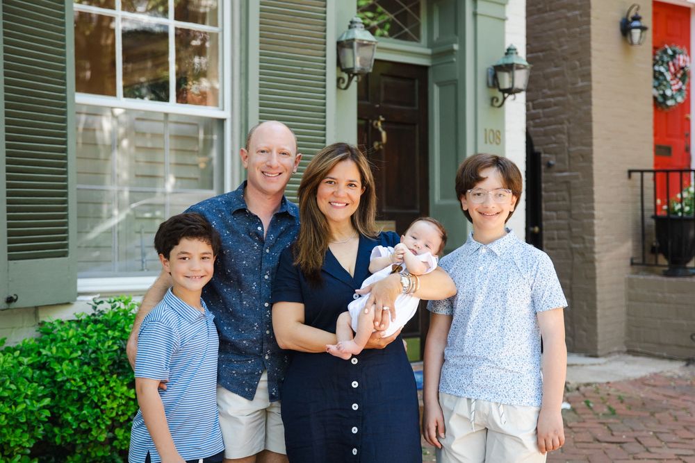 Happy family of five posing outdoors, parents with three children including a baby, dressed in coordinating blue outfits.