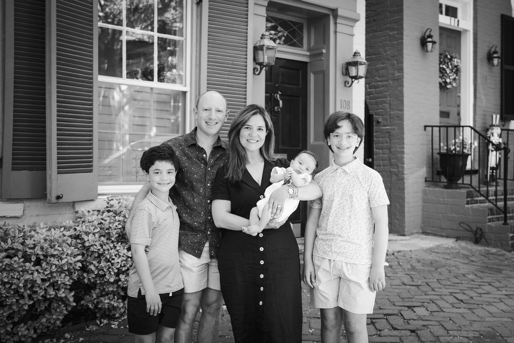 Black and white family portrait of parents with three children posing on brick steps outside a historic home.