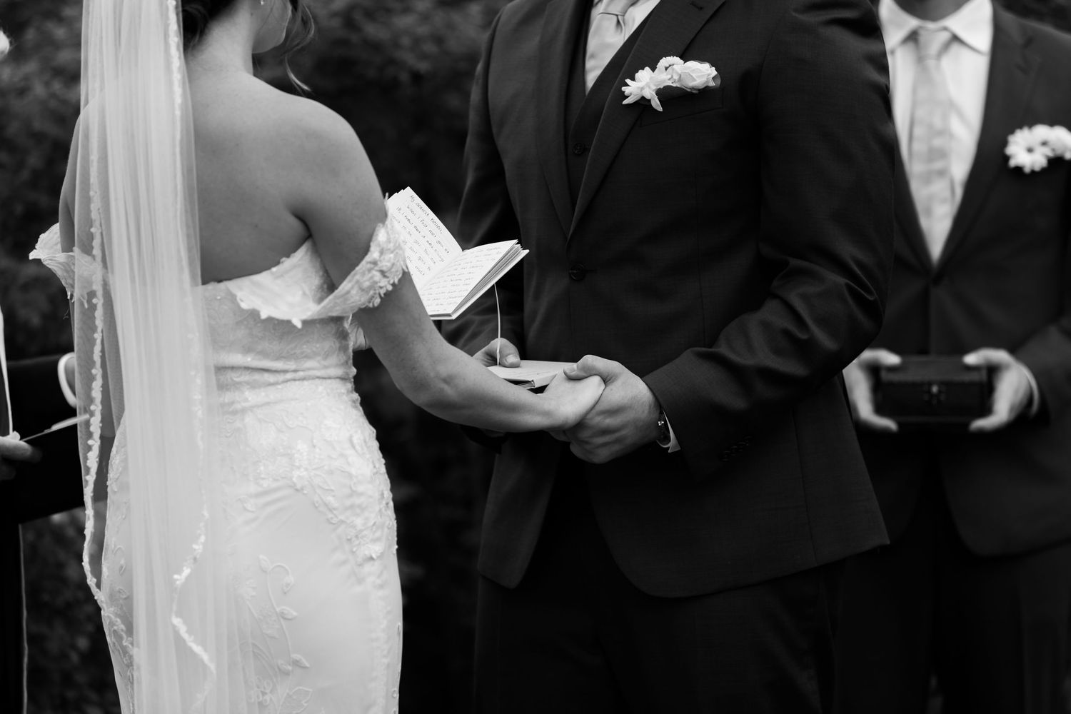 Black and white candid ceremony photo of bride and groom holding hands reading vows at John Hay Estate at The Fells in Newbury, NH