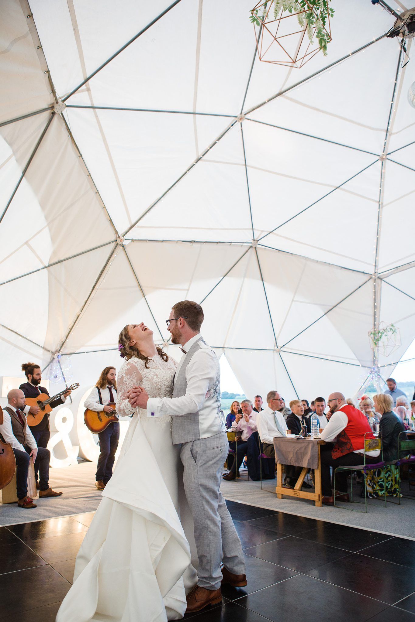 Bride and groom share first dance under geodesic dome tent with live guitarist performing for wedding guests at Oceanstone Resort Wedding