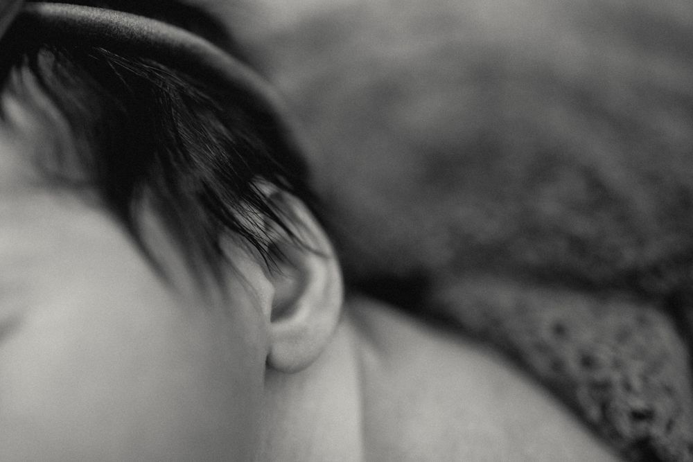 Close-up black and white photo of a newborn baby's ear and dark hair, peaceful and serene.