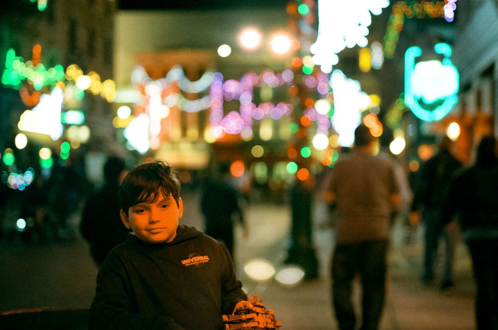 Colorful holiday lights illuminate a festive nighttime street scene.