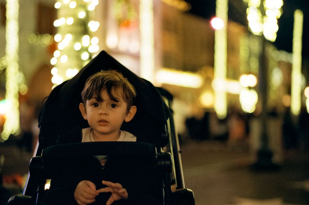 Illuminated nighttime scene with a stroller and holiday lighting displays.