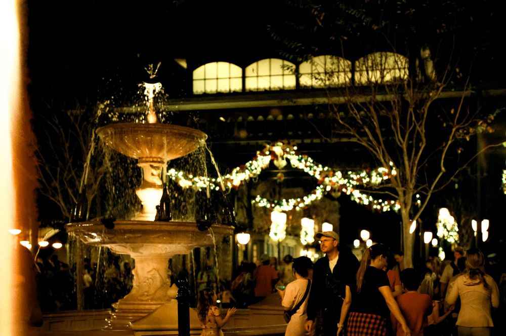 Decorative fountain surrounded by string lights and holiday decorations in an evening plaza.