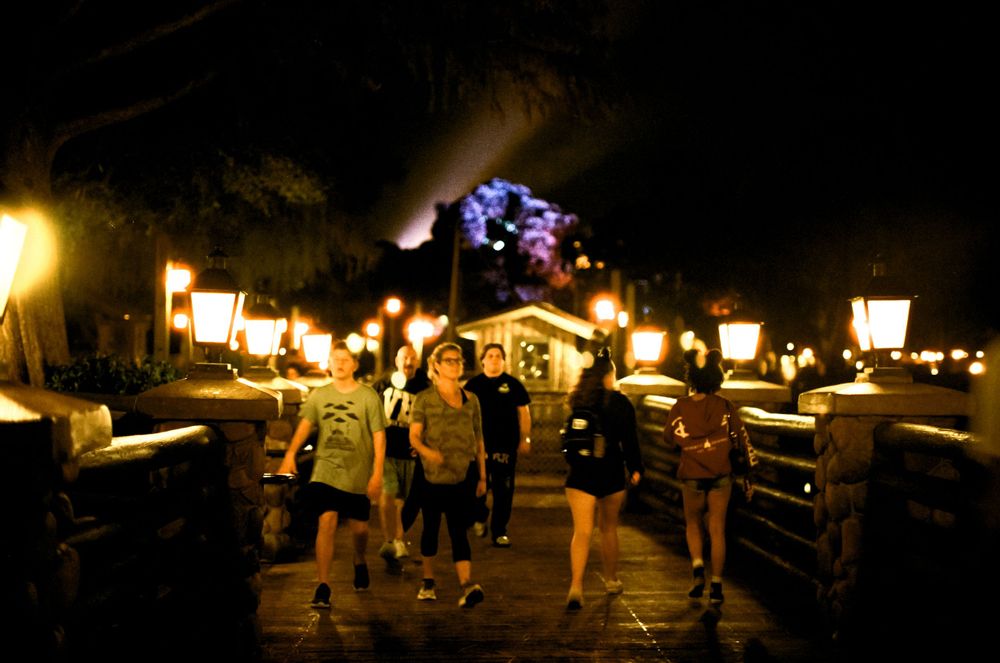 People walking along a dimly lit path with glowing decorations and lanterns.