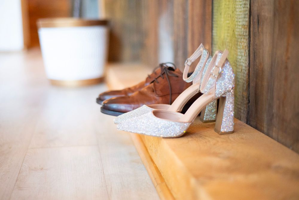A pair of brown leather dress shoes and sparkly heels arranged on a wooden floor.