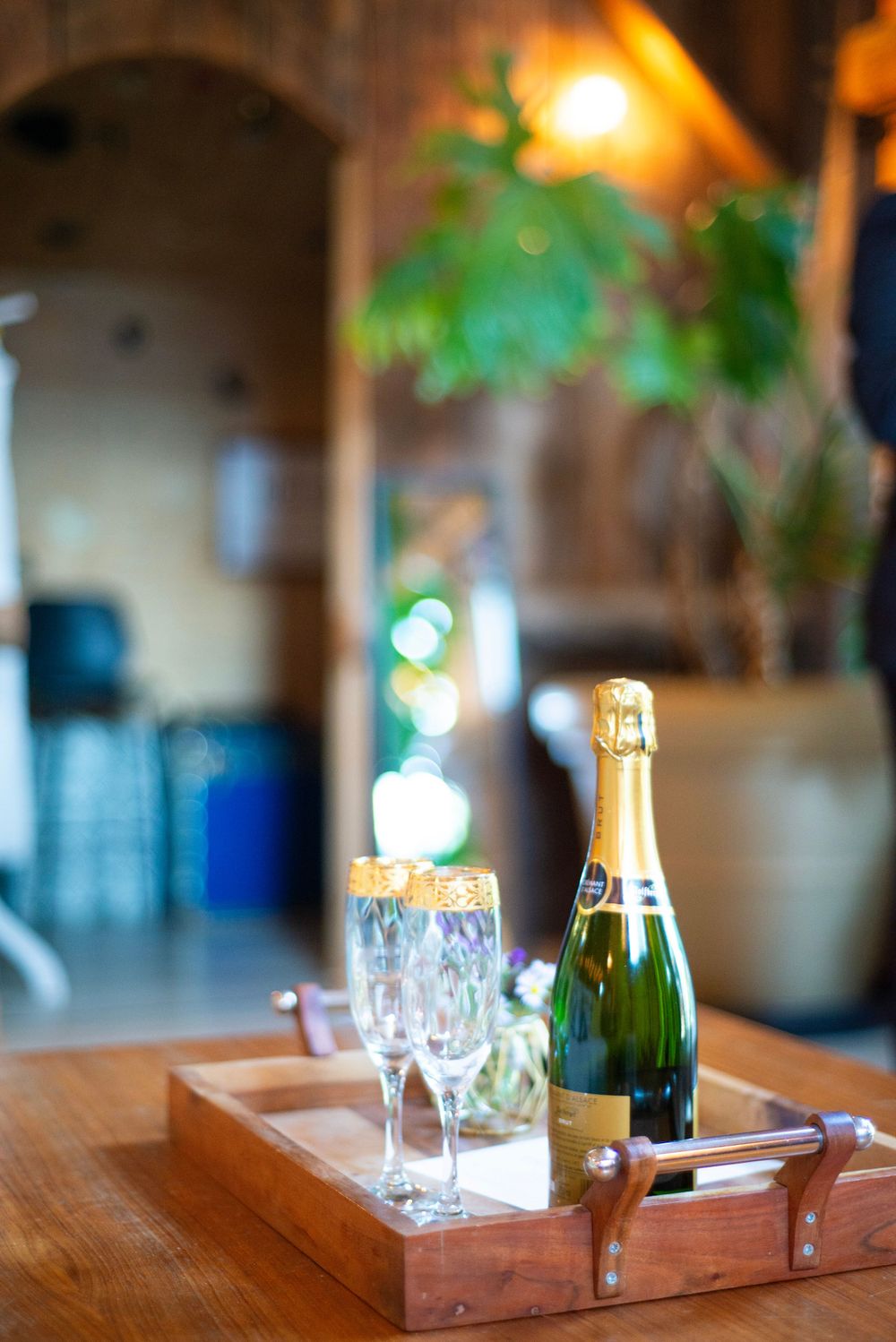A champagne bottle and two crystal glasses sit on a wooden serving tray with ambient lighting in the background.