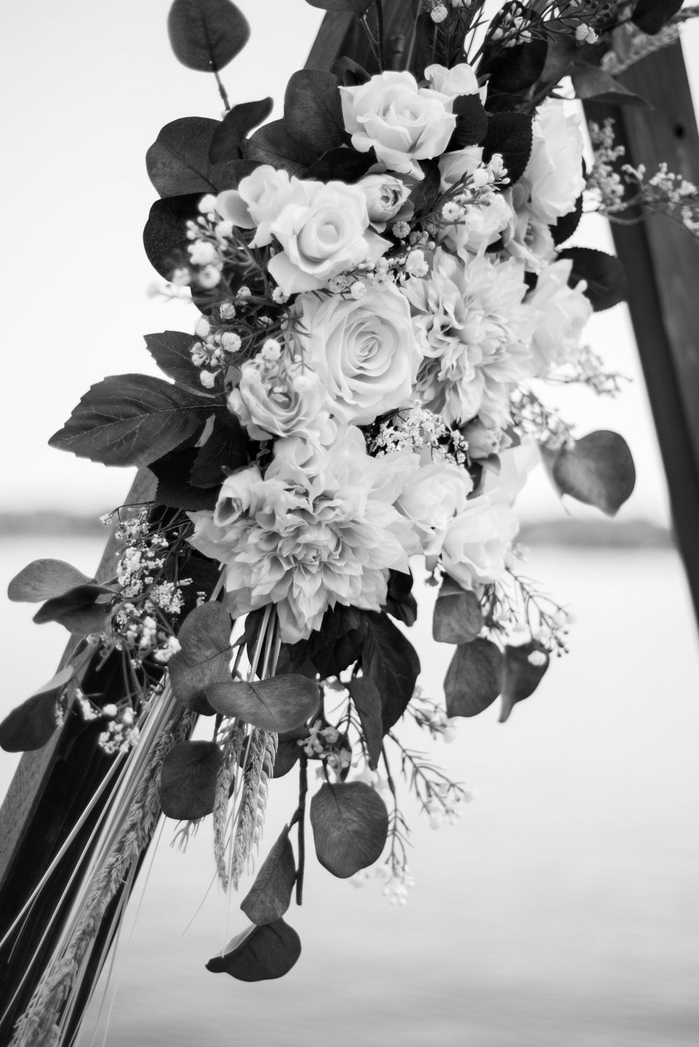 Black and white photograph of an elegant wedding bouquet with white roses and cascading foliage arranged on a dark background.