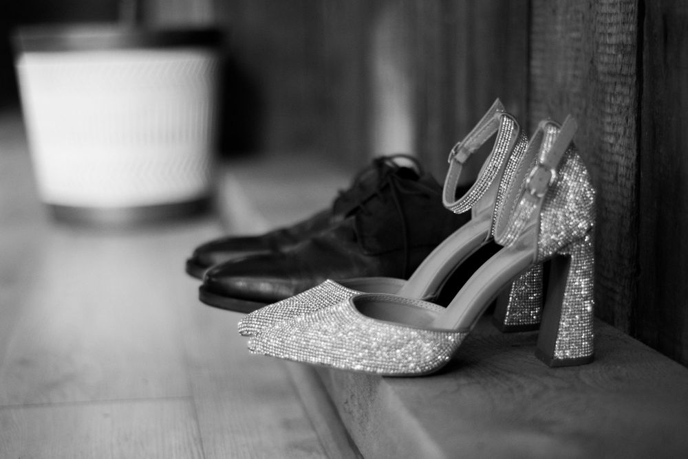 Black and white image of formal wedding shoes with a sparkly heel sitting against a wall.