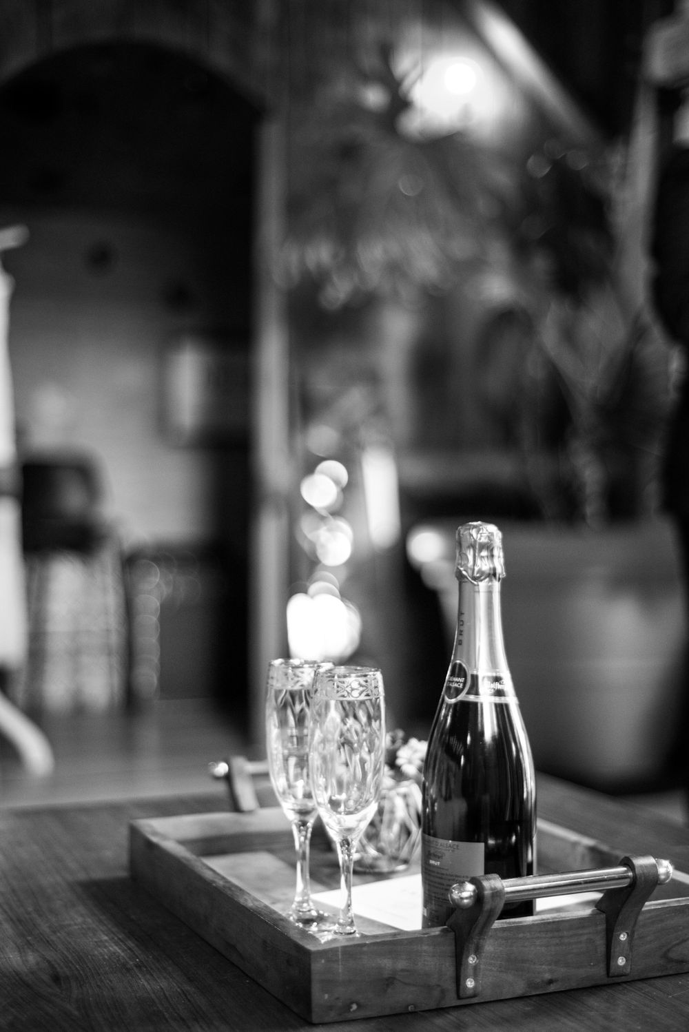Elegant champagne setup with glasses and bottle on wooden tray in black and white photography.