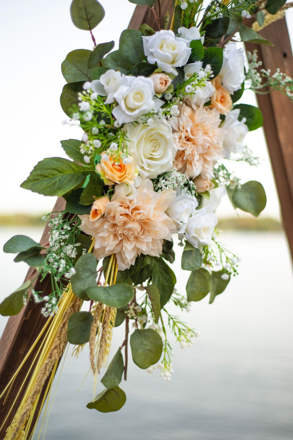 Beautiful wedding floral arrangement featuring white roses, peach dahlias, and eucalyptus leaves cascading down an arch.