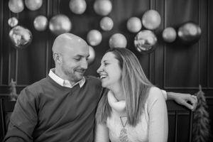 A couple shares a candid moment of laughter together with decorative globe lights in the background.