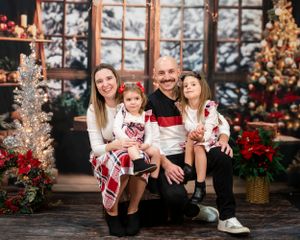 A family wearing coordinated red and white outfits poses for a Christmas photo in a cozy decorated holiday setting.