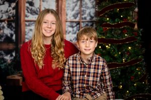 Two people in plaid and red sweater sit together by a decorated Christmas tree in a cozy winter setting.