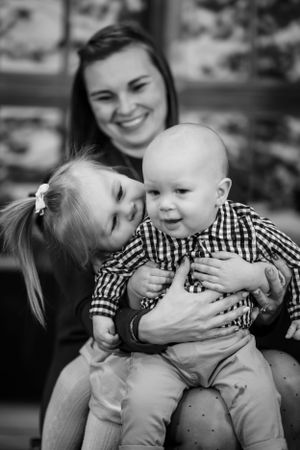 Black and white portrait of a joyful family moment with toddler siblings and parent sharing smiles and laughter.