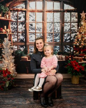A cozy holiday scene with ornate windows, Christmas trees, poinsettias and festive decorations in a rustic wooden setting.