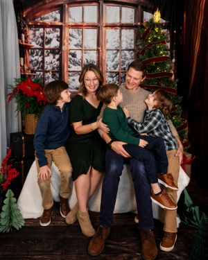 A family gathers for a cozy Christmas photo in front of a decorated tree and window with winter decor.